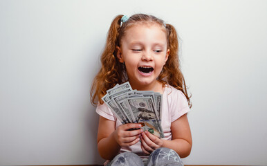 Happy excited emotional kid girl sitting and looking on the money, cash dollars in the hand and joy...