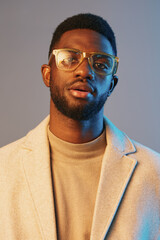Fototapeta premium Stylish young man with glasses in a beige coat, showcasing confidence against a gradient background, ideal for modern fashion concepts and lifestyle branding
