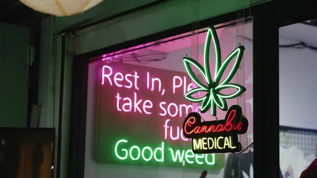 Medical cannabis shop with neon marijuana leaf on the glass showcase on night street of Bangkok, Thailand