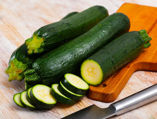 Closeup of fresh courgettes with chopped slices on wooden surface. Vegetarian food concept
