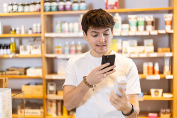 Guy scans the barcode of a package of food supplements in an eco supermarket on mobile phone. Buyer uses a QR code to read detailed instructions and information on how to use the dietary supplement