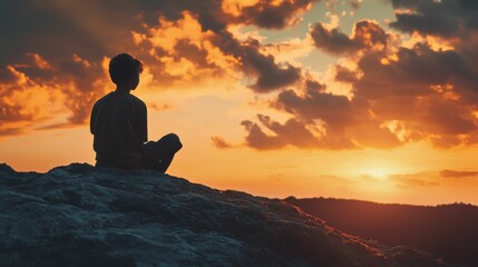 Obraz premium Silhouette of a young boy sitting on a hill top overlooking a sunset