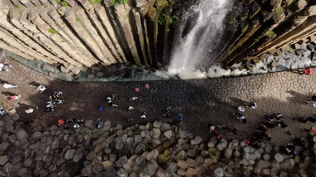 People walk through the canyon and waterfalls of the Huasca de Ocampo Basaltic Prism, Mexico. Drone in overhead view moving laterally through the rock walls