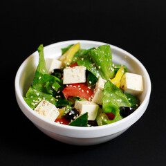greek salad with feta cheese and olives with sesame seeds in a white bowl, shot on a black background with sesame seeds in a white bowl, shot on a black background
