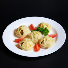 Manti on a white plate, served with tomato wedges and a parsley sprig
