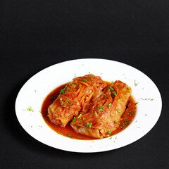 Stuffed Cabbage Rolls with Sauce and Green Onions on a White Round on a Black Background