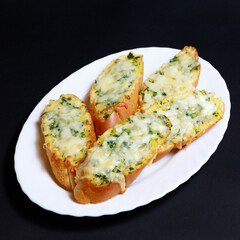Garlic Baguette with Cheese and Herbs on a White Plate with a Black Background