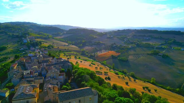 Peaceful aerial truck right pan left shot from Lapedona (FM), the charming town centre with interlocking buildings standing on a hill nestled between gorgeous Marche landscapes, fields, trees, clouds