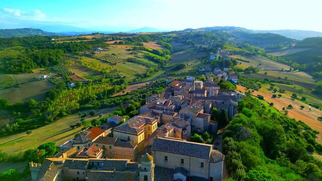 Serene aerial truck left shot from Lapedona (FM), tower, flag, square, bell tower and the town centre's buildings as seen from above, revealing the exquisite detail of the surrounding Marche hillscape