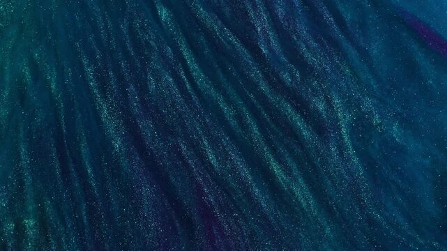 An abstract background of deep blue and green swirls with glitters. The colors blend and flow together like liquid or particles in motion. This combination creates a sense of depth.