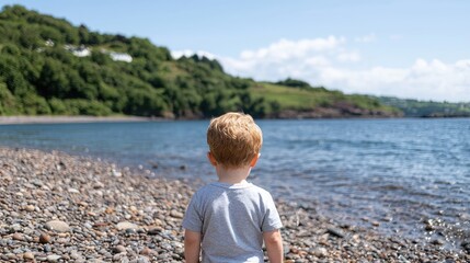 Fototapeta premium Toddler gazing at coastal view, pebble beach, summer