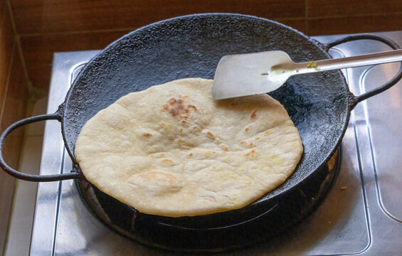 Close-up of homemade bread cooking in an iron tawa, stirred with a steel spatula.