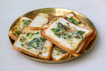 Delicious bread, fried with chilies, onions, eggs, and ghee or clarified butter, is served on a brass plate atop a light wooden surface. This is a very tasty and healthy homemade breakfast.