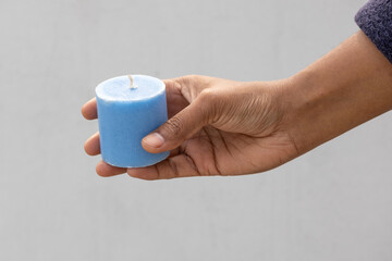 A female hand holds a beautiful blue candle without flame, set against a blurred white background.