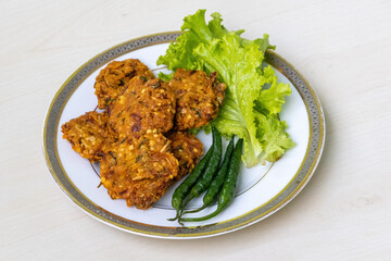 Crispy fried lentil fritters called Piyaju or Daler Bora, served on a white plate against a light wooden backdrop. These onion fritters are a popular Muslim Ramadan snack.