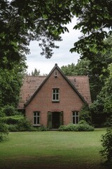 Obraz premium Nestled within a serene, forested area, this historic brick house is enveloped by vibrant, lush greenery, all under an overcast sky