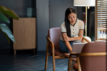 A beautiful, positive Asian woman focuses on working on her laptop in a coffee shop.