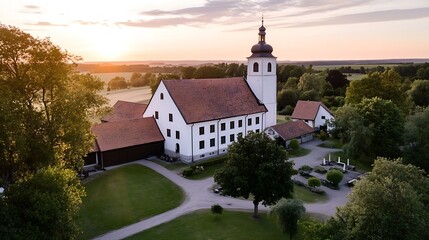 Naklejka premium Aerial view of a quaint white church surrounded by greenery and colorful fields under a sunset sky : Generative AI