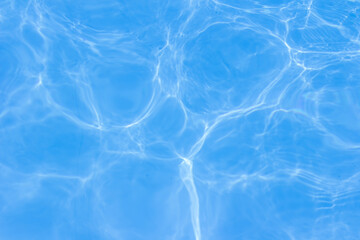 Clear blue swimming pool water surface with sunlight reflections creating abstract patterns and ripples, evoking a refreshing and tranquil summer vibe.