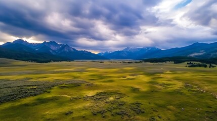 Fototapeta premium Stunning Aerial View of Vast Green Valley Surrounded by Majestic Mountains Under Dramatic Cloudy Sky : Generative AI