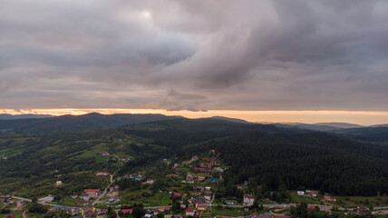 Fototapeta premium Majestic Mountains, Dense Forest, And Dramatic Clouds Illuminated By A Stunning Sunset. Aerial View Capturing The Breathtaking Beauty Of Nature From A Bird’s-Eye Perspective.