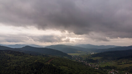 Aerial View Of Majestic Mountains Under A Cloudy Sky At Sunset. The Golden Light Illuminates The Peaks, Creating A Stunning Contrast Between The Dramatic Clouds And Rugged Landscape.
