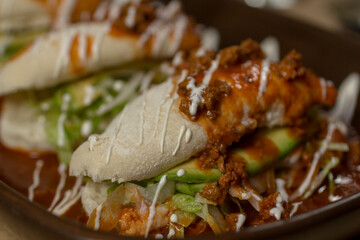 Close-up of Mexican pambazos filled with chorizo, sour cream, and vibrant red sauce, highlighting stuffed layers and fresh, colorful ingredients.