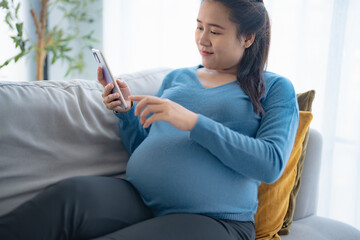 Obraz premium Pregnant asian woman holding smartphone at home using mobile app for pregnant women Positive life moment in pregnancy time