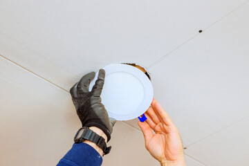 An electrician is carefully placing recessed light fixture into ceiling opening, during home...