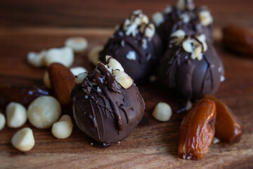 Four chocolate macadamia truffles  with chocolate drizzle sitting on a wooden board with dates and macadamia nuts. 