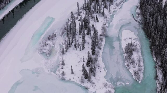 A top-down aerial image of the frozen Takhini River near Kusawa Lake reveals small islands, varying green hues as water turns to ice, and fir-covered forests in a pristine winter landscape.