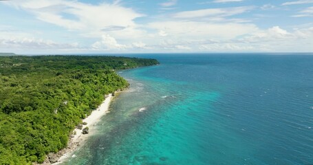 Beautiful sandy beach on a tropical island with abundant green trees along with a small rock formation in the shore.