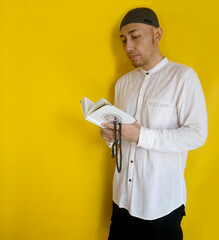 Adult Asian Muslim Man Reciting Holy Book Of Quran With Arabic Letters On The Cover Means Allah Or...