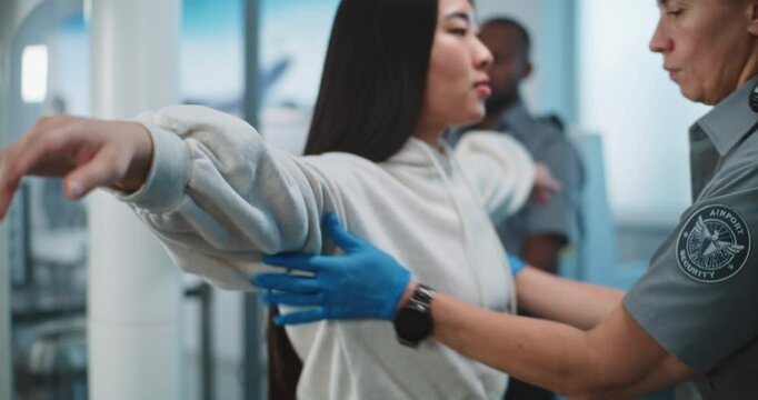 Security Checkpoint in Airport Terminal: Female Security Officer Inspects Asian Woman Body for Suspicious Items for Boarding Plane Flight. TSA Screening Procedures. Tourist Going on Holiday Trip.