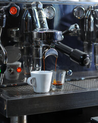 a professional espresso machine pouring fresh espresso shots into a white coffee cup and a measuring glass