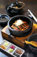 Japanese unagi hitsumabushi dish in a hot stone bowl, accompanied by traditional condiments, sauce, and a teapot