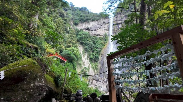 Omikuji fortune telling paper strips hanging near Nachi waterfall with a red bridge in the background, Nachi Katsuura, Japan