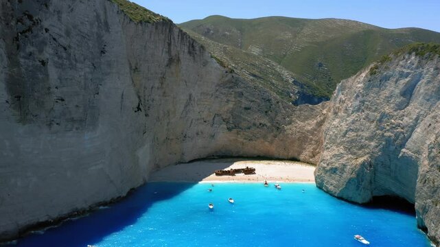 Aerial pullback shot reveals blue sea water landscape of navagio beach or shipwreck beach in Zakynthos coastal island surrounding limestone cliffs