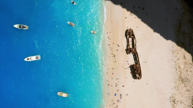 Tourists crowd on navagio beach or shipwreck beach in sunny daylight on Zakynthos coast in Ionian Islands, Greece, Drone view