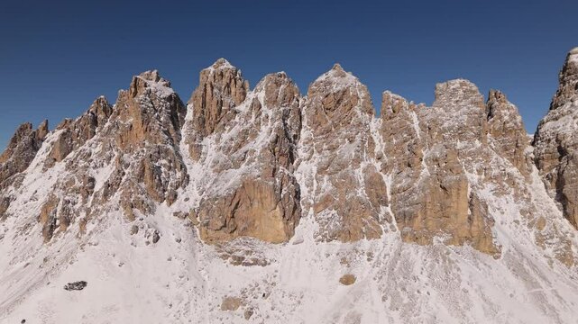 Jagged dolomite peaks form a dramatic rock wall with snow-streaked faces and limestone cliffs rising against a deep blue winter sky