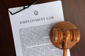 A professional setup featuring an employment law document, a judge's hammer, and glasses on an...