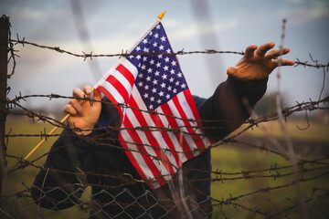 Concept of United States of America closed borders. Sad man at barbed fence., holding USA flag