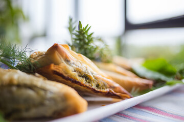 Golden-brown spinach and feta pastry triangles served on a white plate, garnished with fresh herbs,...