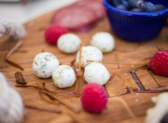 Overhead view of a rustic wooden platter filled with an assortment of charcuterie, cheeses, olives, fresh fruit, and bread, accompanied by wine glasses on a wooden table.