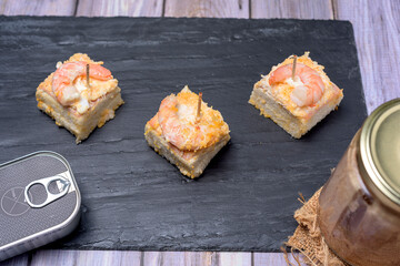 Prawn canape on black slate tray on wooden table with jars and cans of preserves
