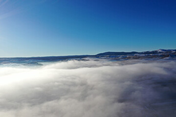 Aerial view of fog blankets during a bright winter morning under a clear blue sky