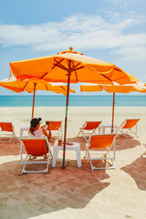 Woman sit on the orange umbrella chair set on the beach with blue sky.