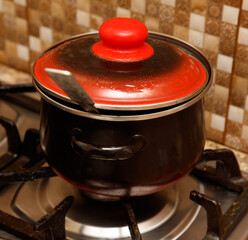 A red and black pot sits on a stove burner