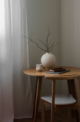 A round ceramic vase with branches, a laptop, a notebook, a coffee mug on a round wooden table in the living room
