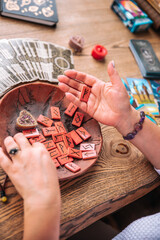 Scandinavian runes in a woman’s hand, tarot cards lie next to her on a wooden table